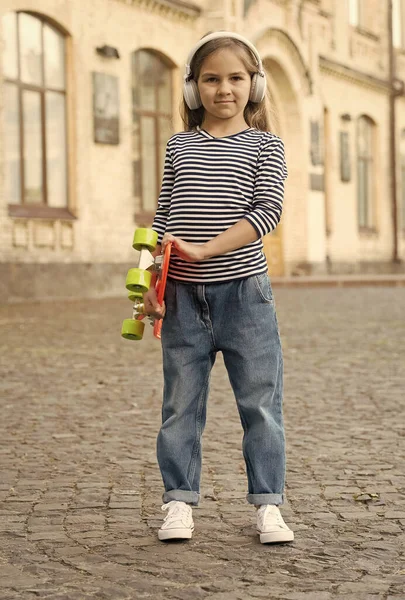 Ragazzina tenere penny board ascoltare musica in cuffie estate urbano all'aperto, viaggiare — Foto Stock