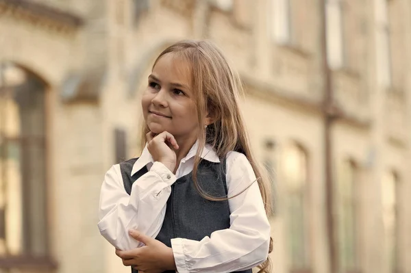 Szczęśliwe małe dziecko zagubione w myślach z troskliwym spojrzeniem w szkolnym mundurze na zewnątrz, myśląc — Zdjęcie stockowe