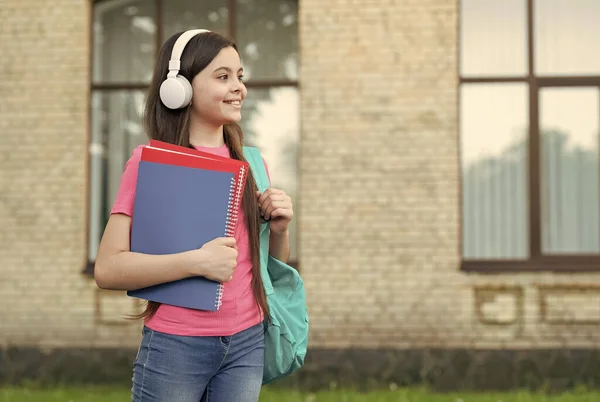 Moderne Grundschule. Glückliche Mädchen tragen Kopfhörer im Freien. Modernes Leben. Kleines Kind hört moderne Musik. Neue Technologie. Lernen und Freude. Modernes Lernen. Modeaccessoires — Stockfoto
