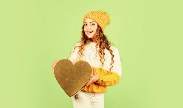 Fijne wintervakantie. Vrolijk klein meisje gebreide hoed en trui. Kind houd hart aanwezig doos groene achtergrond. Valentijnsdag idee. Romantische stemming. Valentijnsdag traditie. Wees mijn valentijn. — Stockfoto