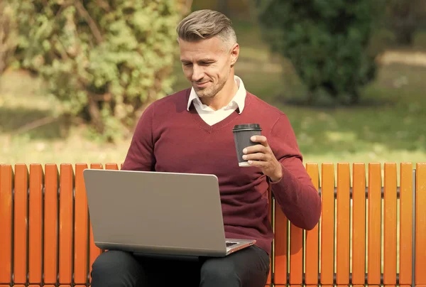 Mooi begin van de dag. Goedemorgen. volwassen knappe man werken op computer outdoor. goed verzorgde man zitten op bank met koffie. Zelfverzekerde zakenman is online. casual zakelijke mode. agile activiteiten — Stockfoto