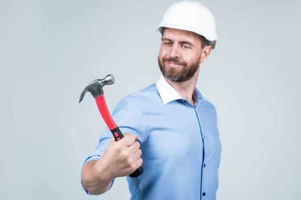 Handsome smiling bearded businessman in helmet hold hammer, repairing — Stock Fotó