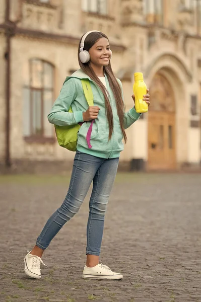 Cuidados de saúde na infância. bebida saudável para adolescente. sentir sede. menina cuidados hidratação corporal. criança ativa e saudável beber água. criança com garrafa de suco em fones de ouvido. de volta à escola. transportar mochila — Fotografia de Stock