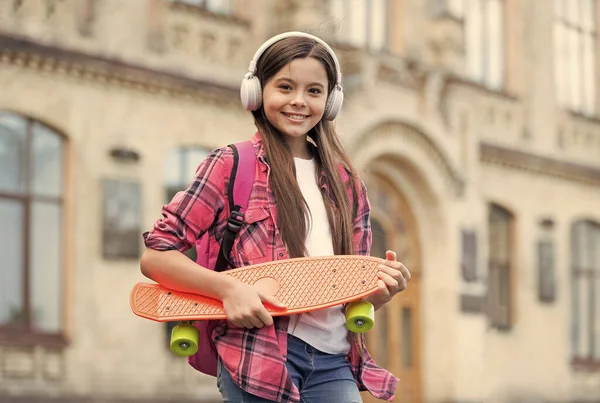 Happy little skater girl hold skating board ouvindo música em fones de ouvido verão urbano ao ar livre, centavo — Fotografia de Stock