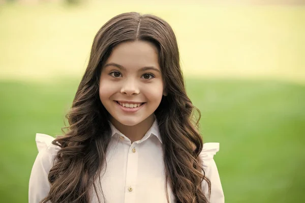 Buon sorriso carino bambino in uniforme scolastica indossando lunghi capelli castani ondulati all'aperto, cura dei capelli — Foto Stock