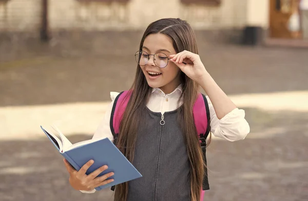 Heureux enfant lire le livre scolaire fixer des lunettes correctrices à l'extérieur, lecture — Photo