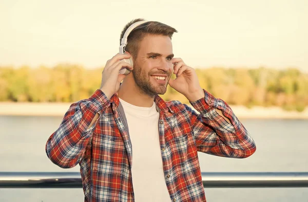 smiling bearded man listen music in digital earphones wearing checkered shirt outdoor, technology