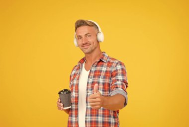 Modern kulaklıklı mutlu adam el hareketi yapıyor. Kahve fincanını onaylıyor ve destekliyor. Zevkle.