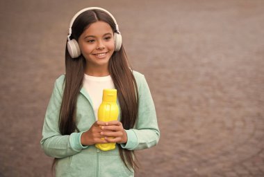 Gençler için sağlıklı bir içki. Formdan sonra susadım. Kız bakım vücut sıvısı. Aktif ve sağlıklı çocuklar su içer. Kulaklığında meyve suyu şişesi olan bir çocuk. Okula dönüyorum. çocuklukta sağlık hizmetleri