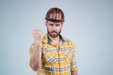 man builder in safety helmet and checkered shirt demonstarte power with fist, male strength.
