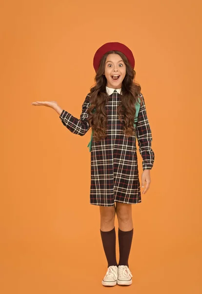 Niño en uniforme de la pupila que presenta el producto. niño en boina francesa sobre fondo amarillo. estudiante universitario adolescente con estilo. Niña con mochila yendo a la escuela. concepto de educación. escuela y moda —  Fotos de Stock