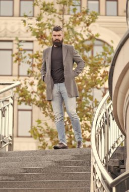 Bıyıklı, vahşi, olgun sakallı bir adam modern, modaya uygun bir ceketle dışarıda yürüyor.