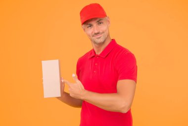 Senin parselin bizim tutkumuzdur. Kurye, parsel kutusunu işaret ediyor. Kırmızı üniformalı teslimatçı, sarı arka planda. Paket teslimat servisi. Paket postası. Her şey kapınızın önünde, boşluğu kopyalayın.