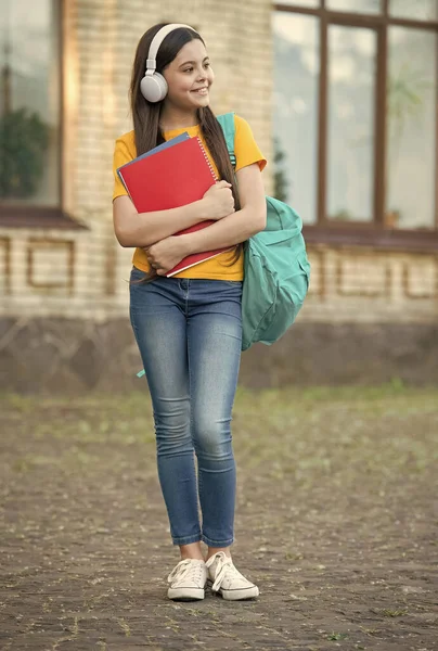 Счастливые девочки носят школьную сумку и книгу в современных наушниках для изучения иностранного языка — стоковое фото