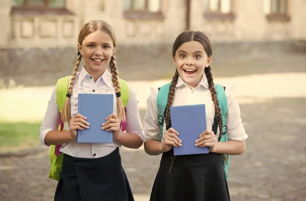 Gran sorpresa para ellos. Chicas felices en uniforme escolar. sorprendido adolescentes estudiantes con mochila celebrar copybook. educación primaria. colegialas aprendiendo juntos. divertirse en el estudio — Foto de Stock