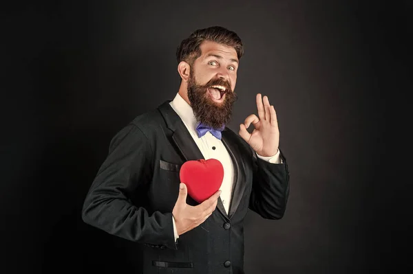 Bonito homem no smoking segurando amor presente de coração para dia dos namorados mostrar ok gesto, valentine — Fotografia de Stock