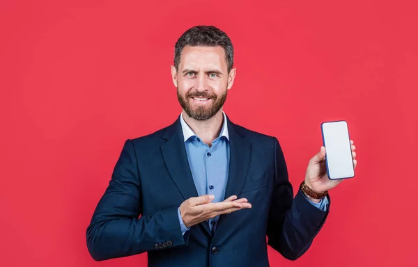 Mature cheerful man businessman in suit presenting product of smartphone, copy space, advert. — Foto Stock