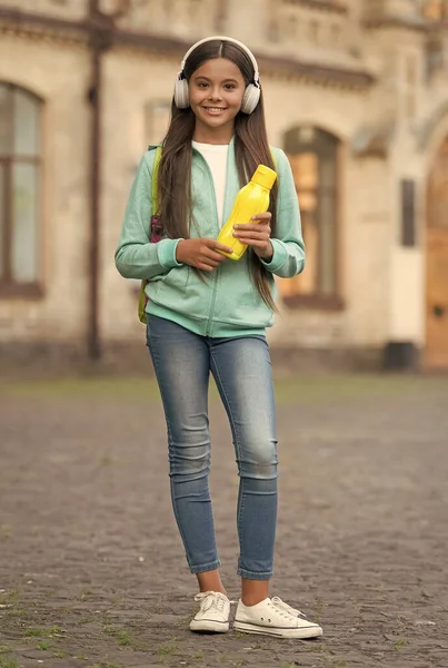 Belo dia. de volta à escola. adolescente menina segurar garrafa esporte. equilíbrio de água no corpo da criança. Hora do almoço. hidratação da saúde. estilo de vida saudável. felicidade infantil. criança feliz usar fones de ouvido ao ar livre — Fotografia de Stock