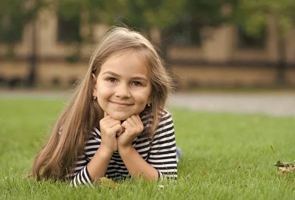 Czuję się wolny. Szczęśliwy uśmiech dziecka leżącego na zielonej trawie. Piękne spojrzenie. Modny wygląd małej dziewczynki. Fryzjer. Pielęgnacja i pielęgnacja włosów. Ubrania dla dzieci. Wakacje — Zdjęcie stockowe