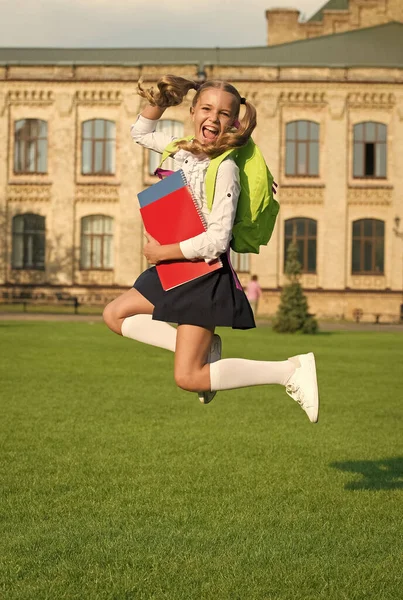 可爱的女孩拿着笔记本跳。快乐的学龄前女孩，校园里有一本书。回学校去努力工作的孩子背着背包。教育的概念。春假时间。暑假 — 图库照片