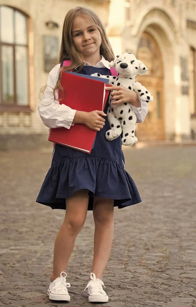 Gelukkig klein kind in schooluniform houden studieboeken en speelgoed hond buiten, 1 september — Stockfoto
