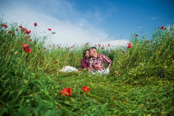 Ζευγάρι στην αγάπη του άνδρα και της γυναίκας πίνουν κόκκινο κρασί στο καλοκαιρινό χωράφι με τα λουλούδια παπαρούνας, ημερομηνία αγάπης — Φωτογραφία Αρχείου