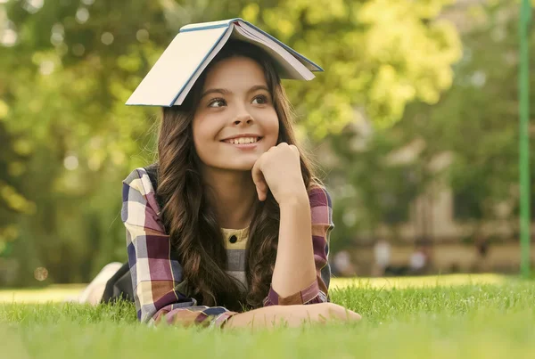 Das ist mein Lesehaus. Glückliches Kind hält Buch auf dem Kopf auf grünem Gras liegend. Leihbibliothek. Lese- und Alphabetisierungskurse. Schulbibliothek. Bibliotheca. Information und Wissen. 1. September — Stockfoto