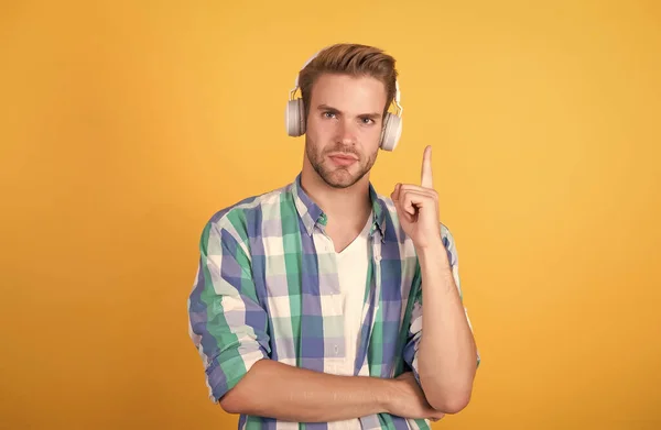 Bel homme porter des écouteurs en gardant doigt levé fond jaune, idée — Photo