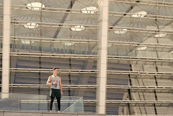 Hombre deportivo sosteniendo botella de agua cerca del gimnasio. joven bebiendo un poco de agua de una botella y descansando después de un entrenamiento. Equilibra tu vida. Mente y cuerpo en armonía. Concepto de estilo de vida de entrenamiento — Foto de Stock