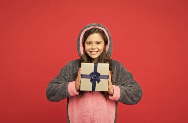 Mutlu çocuk tavşanlı kigurumi giyer ve sürpriz kutusunu tutar. Hediyeler ve hediyeler. Ev aksesuarı hatırası. Dinlenmiş ve mutlu hissediyorum. Dükkan ve alışveriş konsepti. Tavşan pijamalı genç kız. İyi alışverişler.