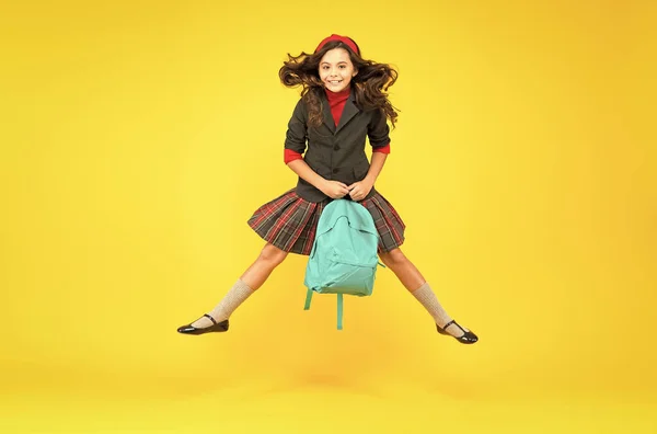 Boldog kis gyerek formális egyenruhában tartja iskolai táska ugrás a levegőben sárga háttér, iskoláztatás — Stock Fotó