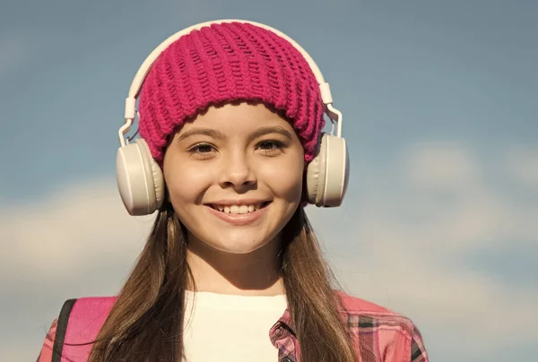 Protege tus orejas de niño. Chica feliz usar auriculares en el cielo azul soleado. Los niños escuchan música en los auriculares. Cuidado del oído y la audición. La vida moderna. Nueva tecnología. Mantenerte entretenido y seguro — Foto de Stock