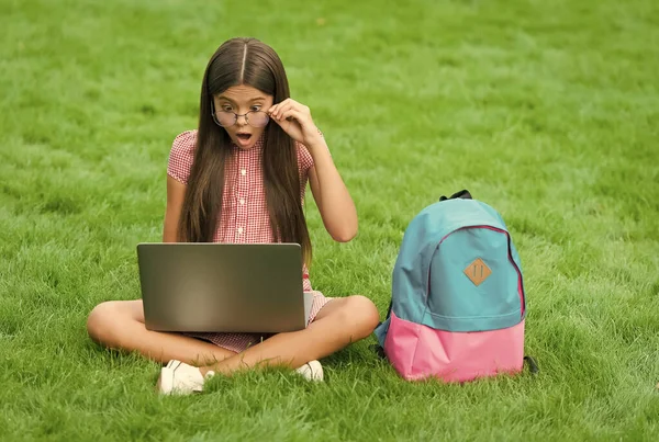 Bambino sorpreso in occhiali guardando lo schermo durante la riproduzione di giochi per computer sul computer portatile nel parco, intrattenimento infantile — Foto Stock