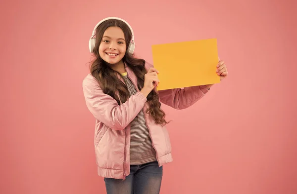 Fröhliches Kind trägt Kopfhörer und zeigt leeres Papier für Kopierraum, Werbung — Stockfoto
