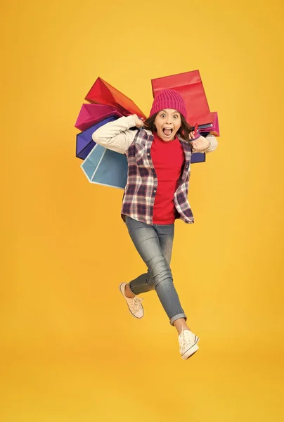 İstediğin şey için alışveriş yap. Enerjik çocuk alışveriş torbalarını sarı arka planda taşır. Satış ve alışveriş. Siber Pazartesi. Kara Cuma. Moda eğlenceyle buluşur — Stok fotoğraf