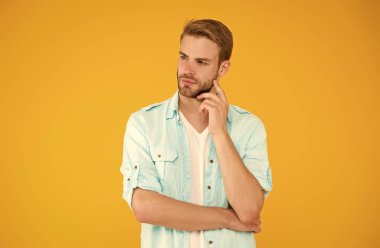 Düşünceli adamın sarı arka planda saçları var. İnsani duygular. Havalı saç stili olan seksi çocuk tişört giyiyor. Tıraşsız, tüylü yakışıklı bir adam. Erkek yaz modası. Seksi maço adam.