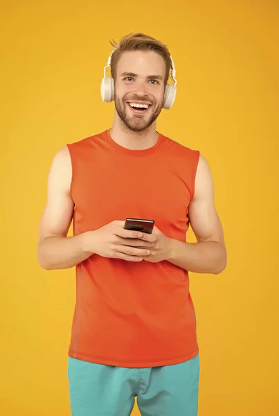 Feliz joven en ropa deportiva usar auriculares modernos escuchar música mientras el uso de entrenamiento smartphone, aplicación de compras de fitness — Foto de Stock