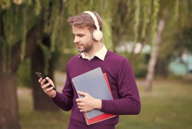 Kısa mesaj okunuyor. Adam not almak için defteri tutuyor. Faydalı bilgi almak. Adam okumayı seviyor. Öğrenci hayatı. Kitaplı eğitim. Kulaklıklı akıllı adam cep telefonundan müzik dinliyor.