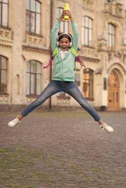 Zıplayan mutlu çocuk dışarıda su şişesiyle özgürlük ve neşe hissediyor, aktif ve enerjik bir çocukluk geçiriyor.