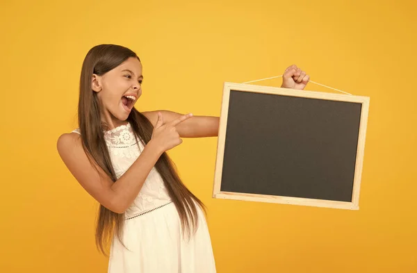 Retour à l'école. espace de copie. vacances d'été et vacances. bonne enfance. petite fille pointant du doigt tableau noir. mode pour les enfants. petit enfant sur fond jaune. activité de camp d'été. L'excitation — Photo