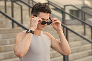 Şık bir spor modası ve güneş gözlüğü. Yakışıklı adam spor kıyafetler giyiyor. Saati olan bir sporcu. Fitness erkek sporcusu dışarıda antrenman yapmaya hazır. Erkek spor modası. Güçlü ve kaslı.