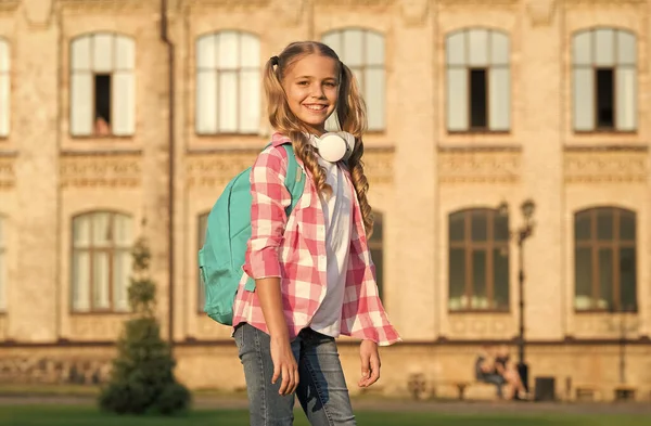 Niña pequeña usar camisa a cuadros. niño con auriculares al atardecer. moda de primavera y verano para niños. Feliz infancia. e-learning con ebook. tecnología moderna. alegre amante de la música con mochila — Foto de Stock