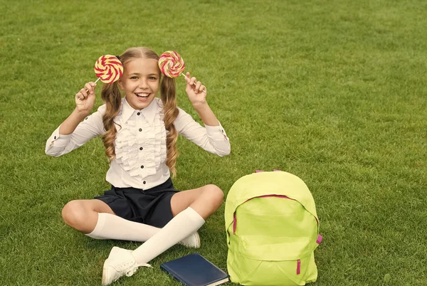 A educação dá doce. criança engraçada segurar pirulito. conceito de educação. dia de aprendizagem comum. menina bonito ler livro após lição. menina pré-escolar feliz com livro no quintal da escola. voltar para a escola — Fotografia de Stock