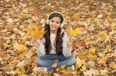 Dinlenme zamanı. Online eğitim. çocukluk mutluluğu. Güzellik ve doğa. Mutlu çocuk kulaklık takıyor. Genç kız okula giderken müzik dinler. Çocuk sonbahar ormanında rahatlar. Sonbahar akçaağaç yaprakları parkta