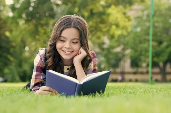 Chcete-li uspět, musíte číst. Šťastné dítě čte knihu ležící na zelené trávě. Školní knihovna. Vzdělání o gramotnosti. Doma. Lekce literatury. Učím se cizí jazyk. Anglická škola. Stojí za to strávit čas — Stock fotografie