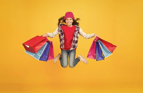 Gelukkig klein meisje springen met boodschappentassen gele achtergrond, verkoop — Stockfoto