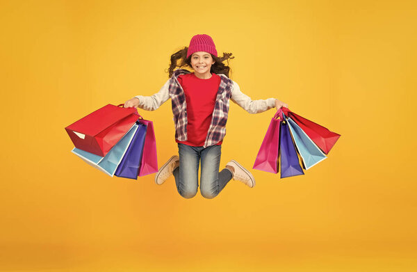 Happy little girl jump with shopping bags yellow background, sale