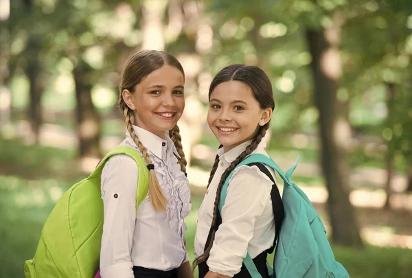 Amigos inteligentes. de volta à escola. as meninas de escola pequenas andam na primavera. feliz dia das crianças. felicidade infantil. duas irmãs de uniforme escolar ao ar livre. Pronto para as férias. feliz adolescente crianças carregam mochila — Fotografia de Stock