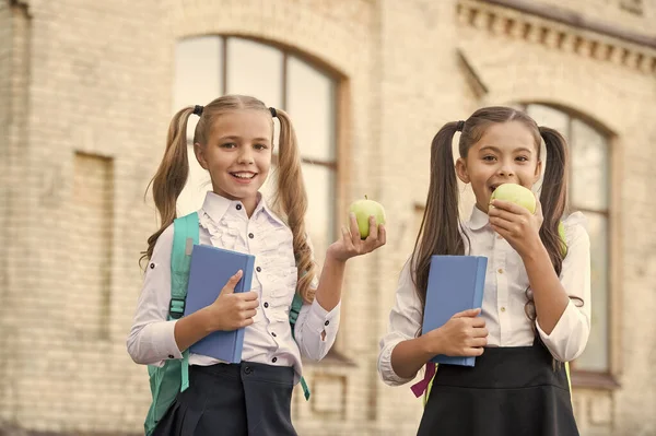 Учащиеся одноклассницы с рюкзаками, обедающие в школе, поедающие яблоки — стоковое фото