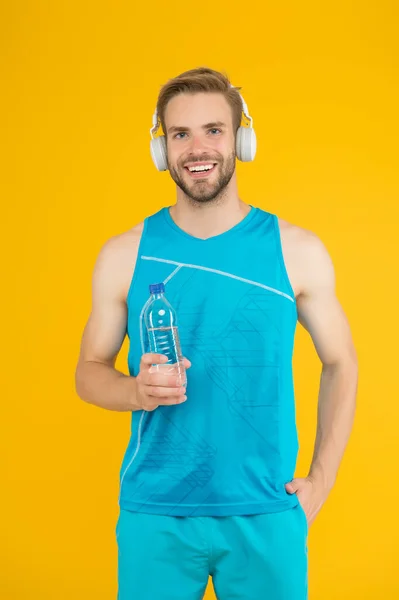 Keep body and mind in good shape. Happy sportsman hold water bottle. Fitness trainer. Feeling thirst. Thirst and dehydration. Thirst control. Drinking water. Cheerful athletic guy listening music